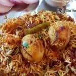close-up of egg biryani served in a plate with raita and sliced onions