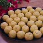 besan ladoo placed in a black color plate over brown counter top, garnished with cashews.