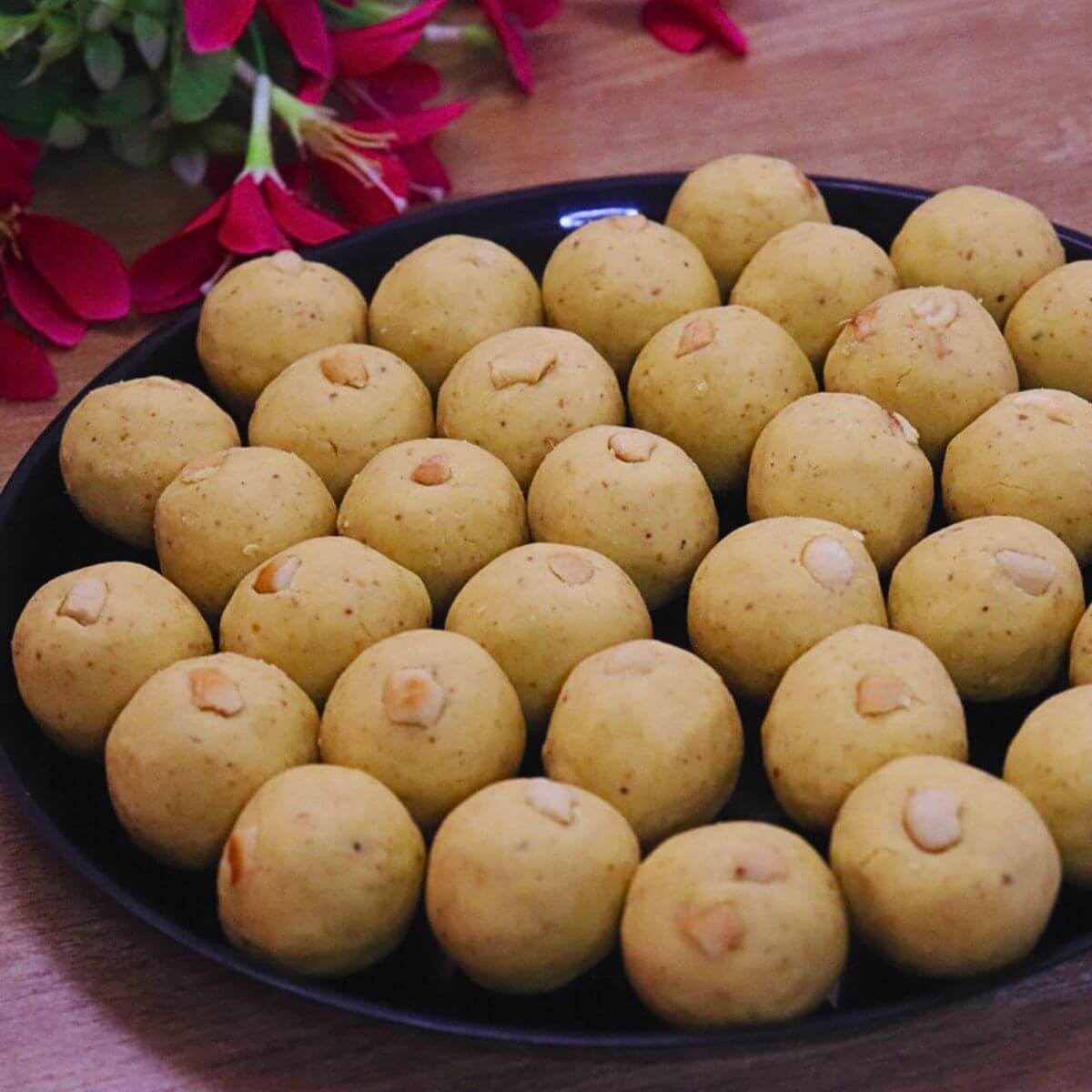 besan ladoo placed in a black color plate over brown counter top, garnished with cashews.