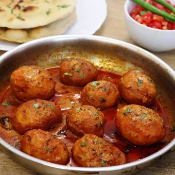 close-up of kashmiri dum aloo in a skillet. Garnished with fresh coriander leaves.