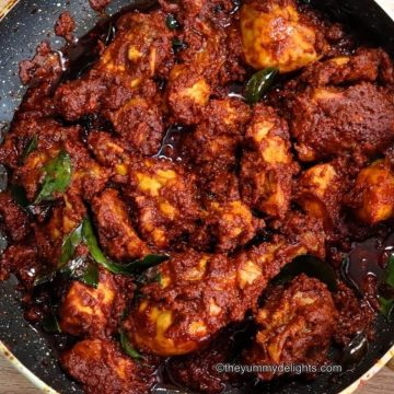 close-up image of mangalorean chicken ghee roast. It shows succulent pieces of chicken coated with ghee roasted masala in a black color pan.