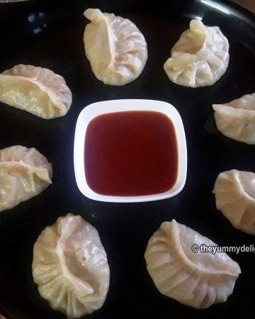 Veg momos served in a plate with spicy tomato sauce.