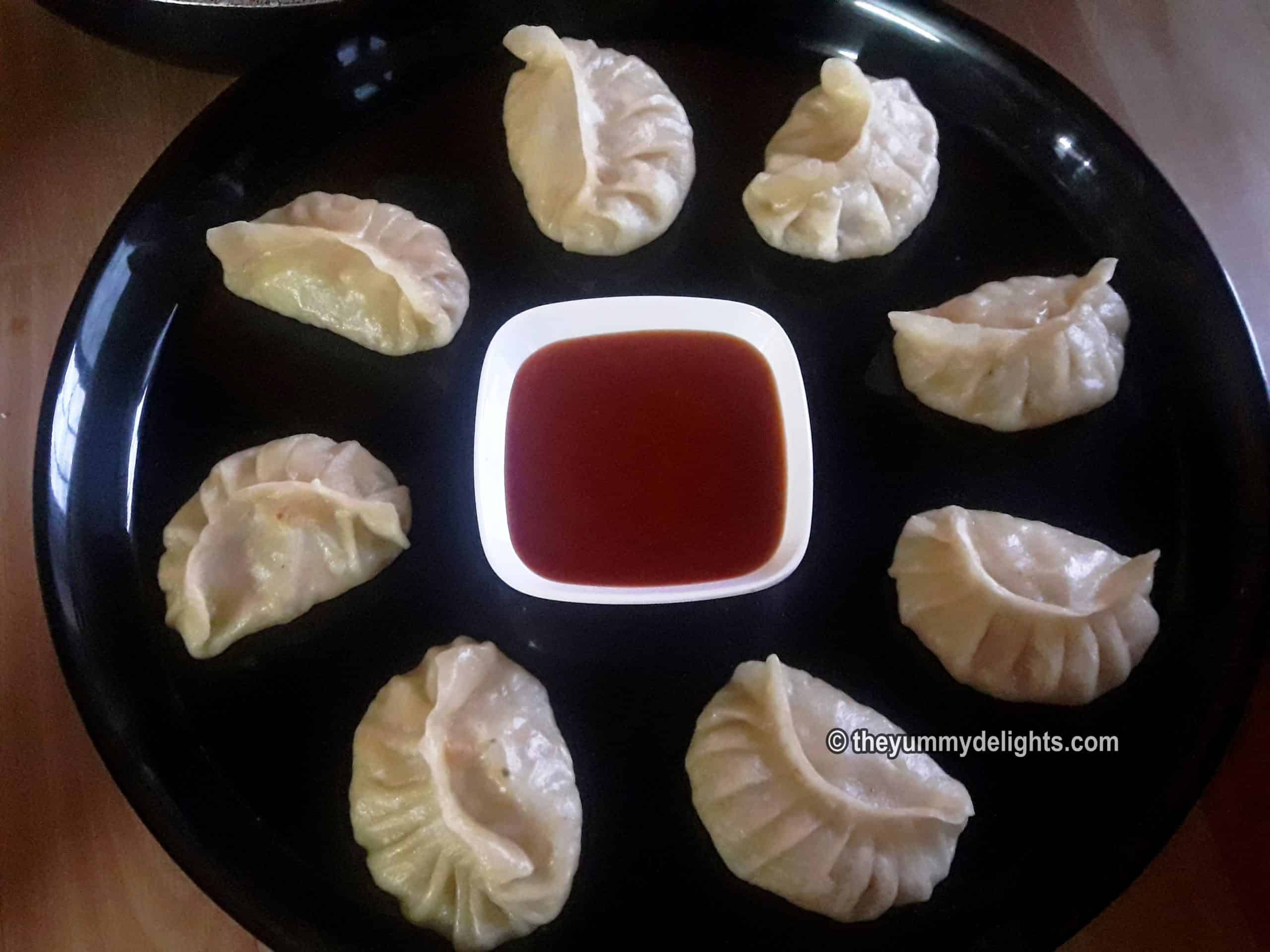 Veg momos served in a plate with spicy tomato sauce.
