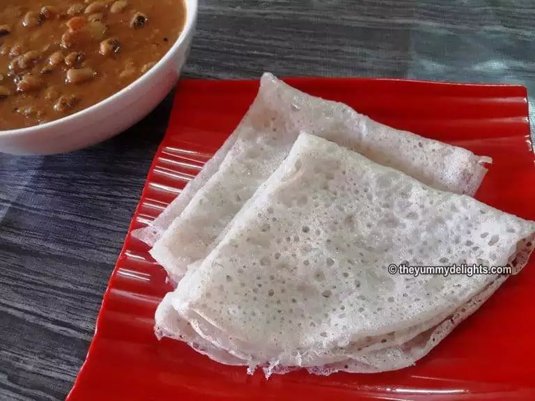 close-up of 2 neer dosa folded and served on a red color plate.