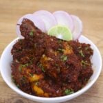 kolhapuri chicken sukka served in a white bowl with onion rings and a lemon wedge.