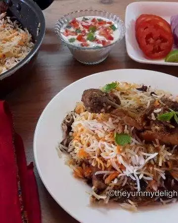 lucknowi chicken biryani served in a white plate with salad & raita.
