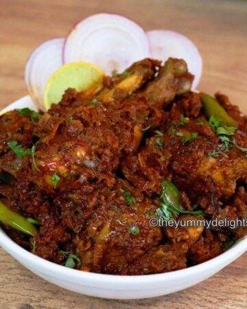 Chicken masala served on a white plate with onion slices & lemon wedge.