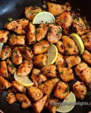 garlic butter chicken bites in a pan garnished with lemon wedges & cilantro. Close up image.