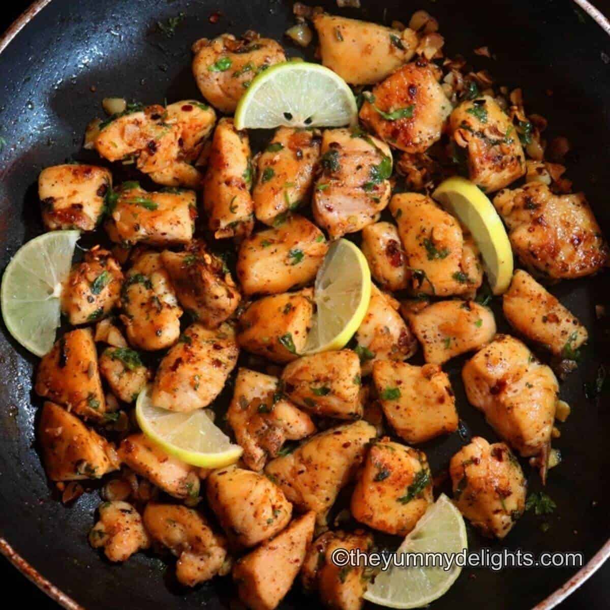 garlic butter chicken bites in a pan garnished with lemon wedges & cilantro. Close up image.