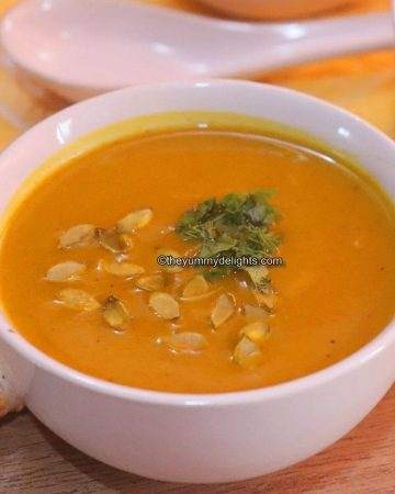 pumpkin soup served in a white bowl. Garnished with toasted pumpkin seeds & cilantro leaves.