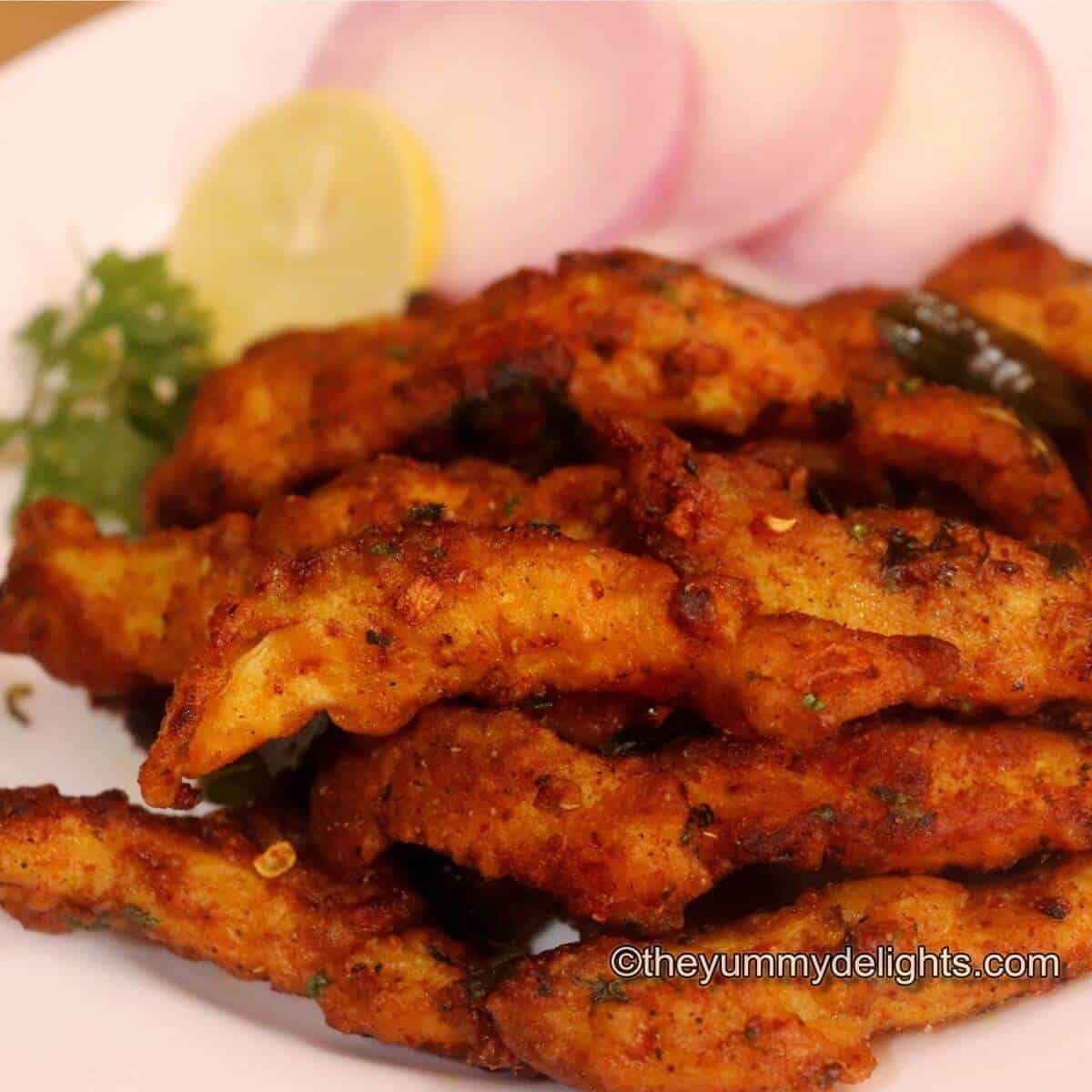 Hyderabadi chicken majestic served on a white plate. Served with onion slices, lemon wedge & coriander leaves.