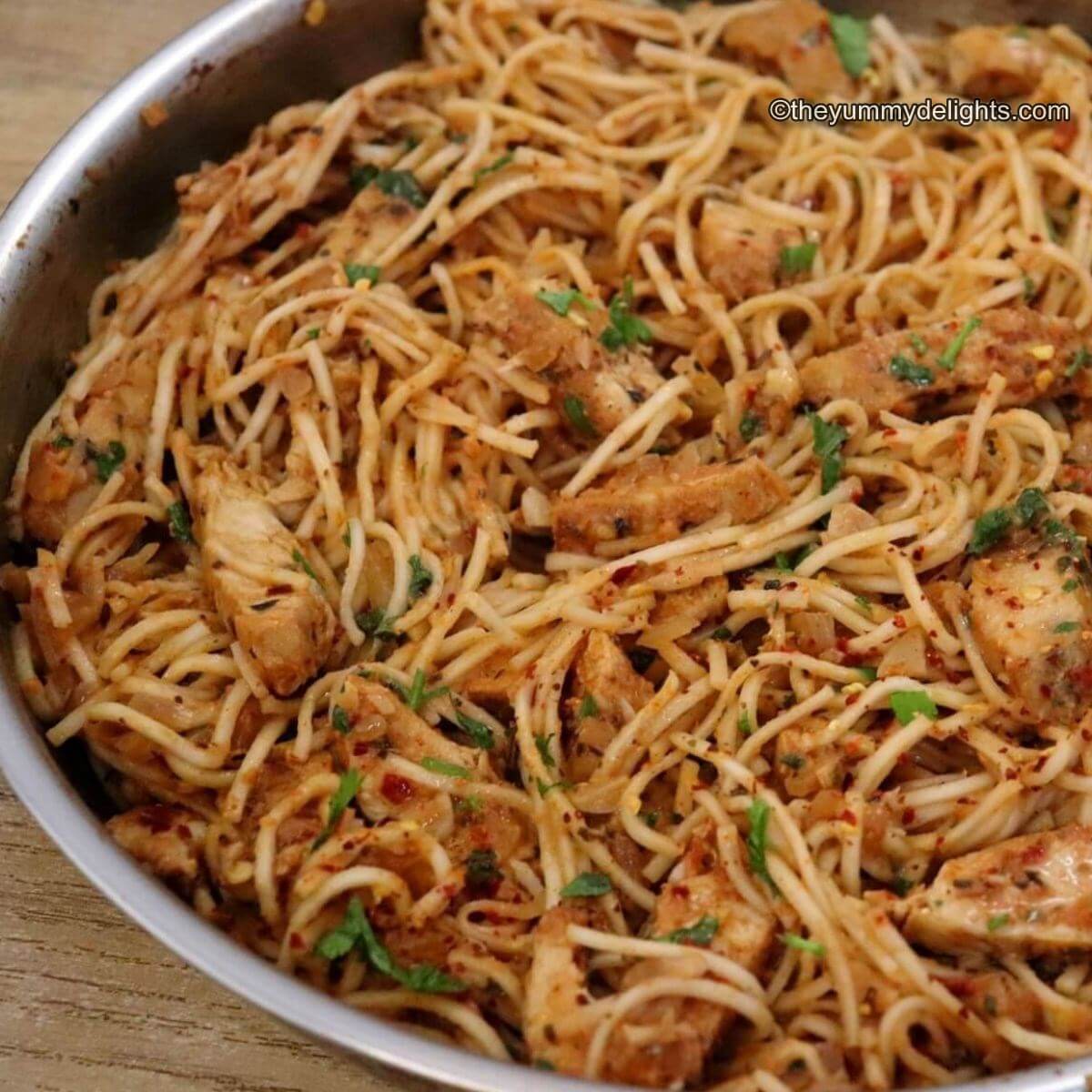 close-up of spicy chicken spaghetti in a skillet. This spicy chicken pasta is garnished with Parmesan cheese, parsley and a dash of red pepper flakes.