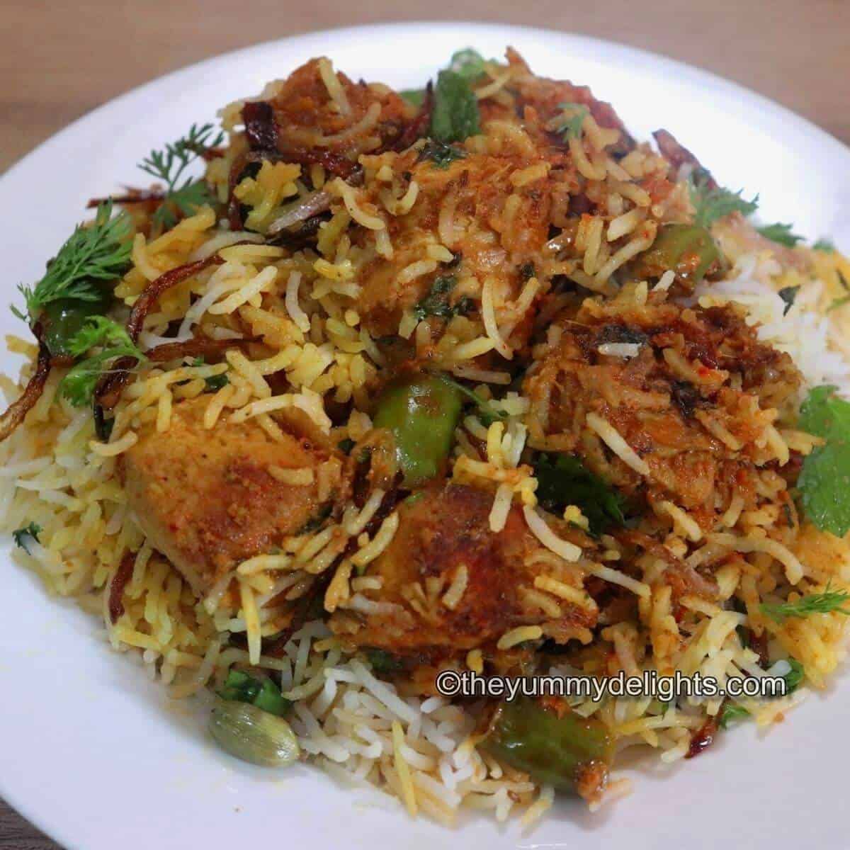 close-up image of chicken tikka biryani served in a white plate. Garnished with fried onions, mint and coriander leaves.