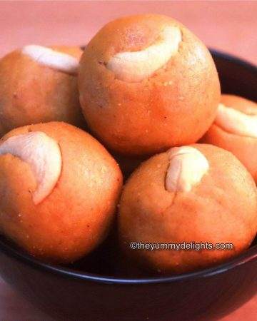 Moong dal ladoo close-up image. The ladoo are served in a black bowl & garnished with cashews.