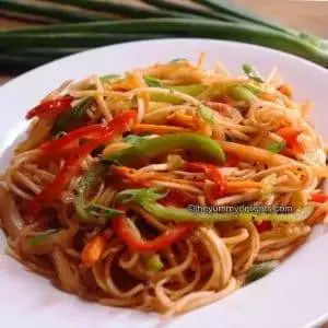spaghetti marinara served in a white plate. Garnished with spring onion greens.