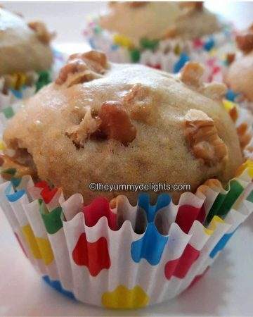 Eggless banana nut muffins placed on a white plate. A few banana muffins are placed nearby.