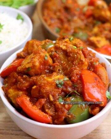chicken jalfrezi served in a white bowl with stir-fried bell pepper and onions. Chicken Jalfrezi is garnished with coriander leaves.