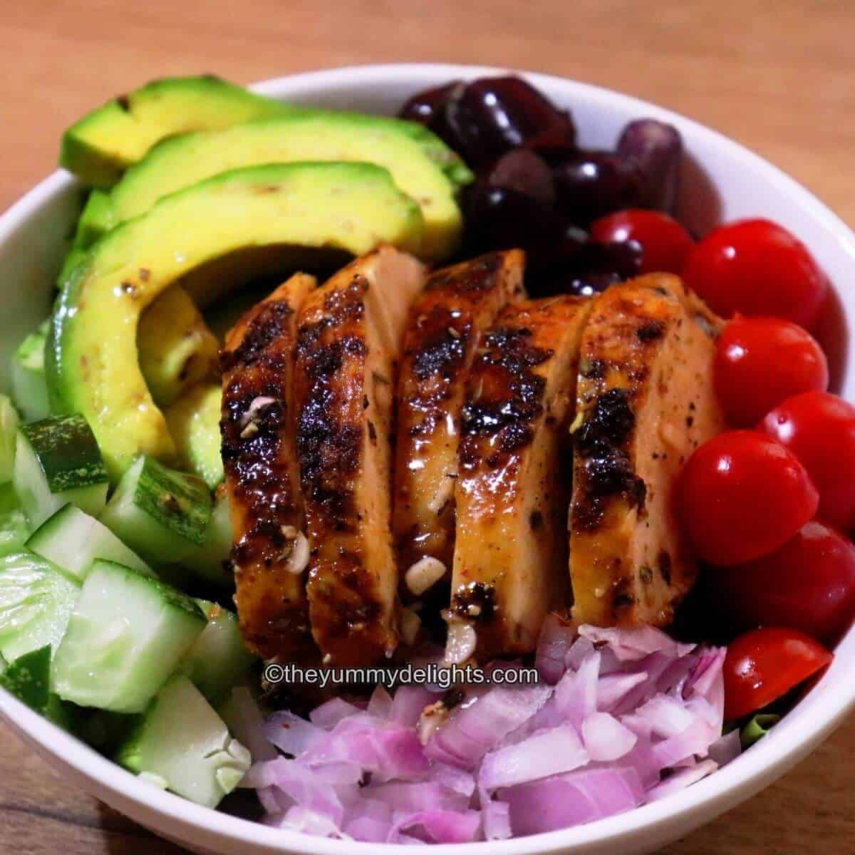 summer grilled chicken salad served in a white bowl with fresh fruits and vegetables.