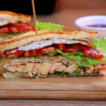 close-up of chicken club sandwich sliced in half and placed on a board.