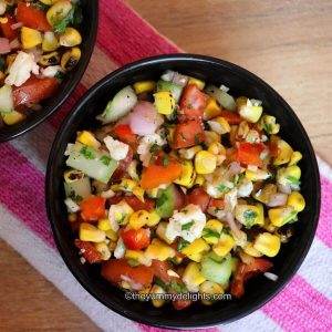 close-up of grilled corn salad in a black bowl. Another black bowl with corn salad is placed nearby.