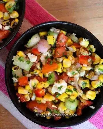 close-up of grilled corn salad in a black bowl. Another black bowl with corn salad is placed nearby.