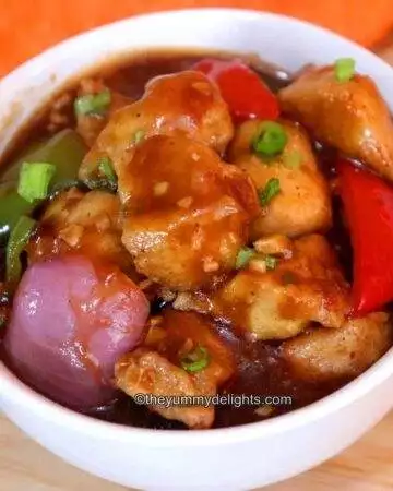 Chicken manchurian gravy served in a white bowl. This chicken manchurian is garnished with spring onion greens.