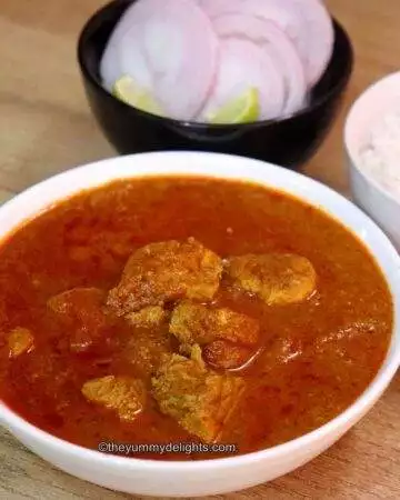 gavran chicken curry served in a white bowl. Served with steamed rice in a white bowl with onion rings and lemon wedge on the side.