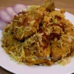 Kolkata chicken biryani served on a white plate with sliced onions and lemon wedge the side.
