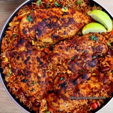 Close-up image of Mexican chicken and rice in a pan garnished with cilantro and lemon wedges.