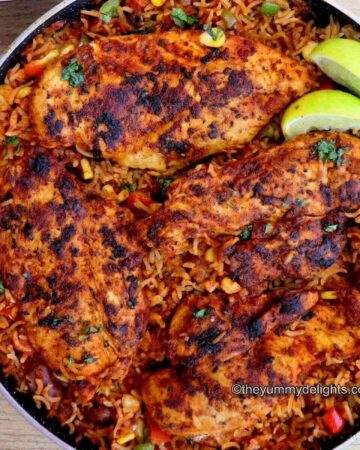 Mexican chicken and rice in a pan garnished with cilantro and lemon wedges.