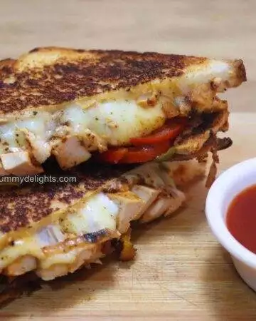 chicken fajita sandwich placed on a chopping board. On the side, tomato sauce is kept on a small white bowl.
