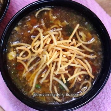 close-up of chicken Manchow soup in a black bowl with crispy fried noodles on the top.