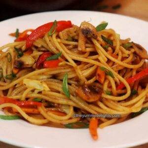 vegetable lo mein served on a white plate garnished with spring onion greens.