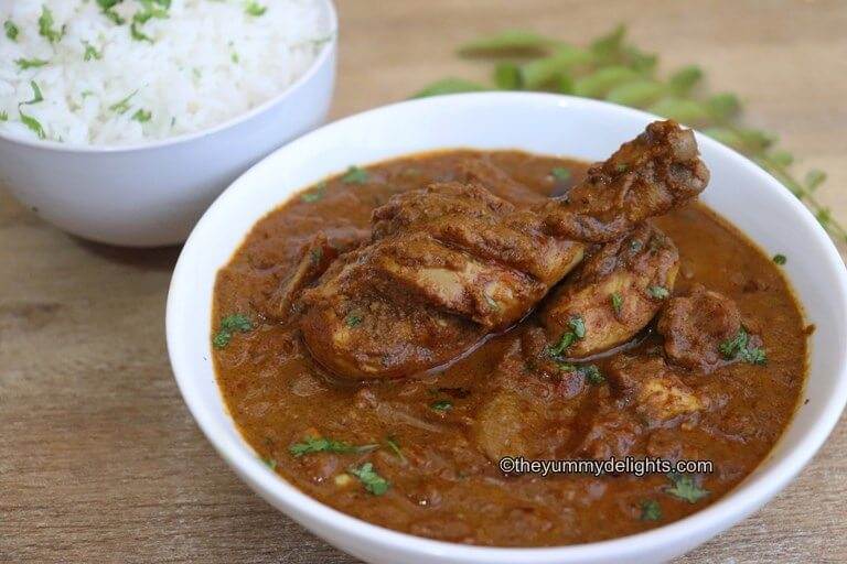 Chettinad chicken curry served in a white bowl. Another white bowl, full of steamed rice is placed on the side.