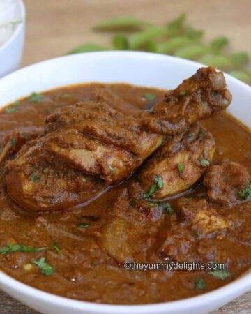chicken chettinad gravy served in a white bowl. Garnished with curry leaves and coriander leaves.
