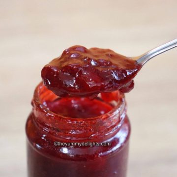 close-up of spoon full of strawberry jam placed on a strawberry jam jar.