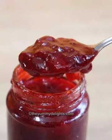 a spoon full of homemade strawberry jam taken out from a jar filled with jam.