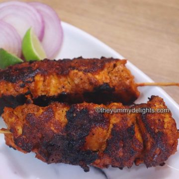 chicken boti kabab served on a white plate with lemon wedge and onion slices.