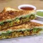 close-up of grilled tandoori chicken sandwich served with green chutney and tomato sauce on the side.