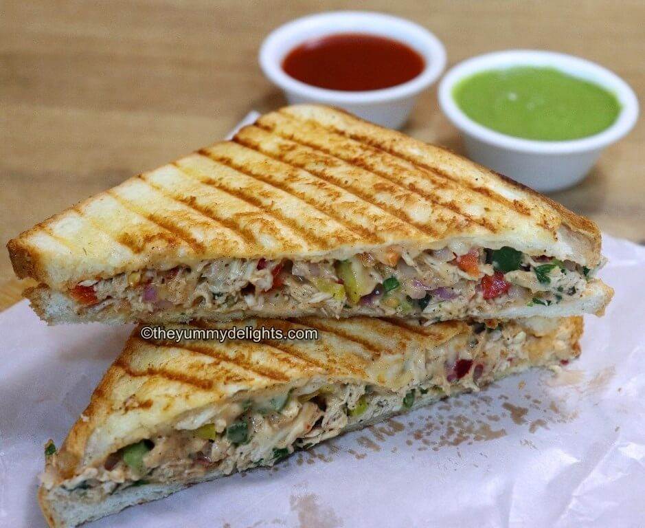 close up image of cheesy shredded chicken sandwich served with tomato sauce and green chutney.