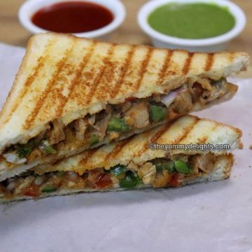 side view of grilled chicken sandwich served with tomato sauce and green chutney on the side.