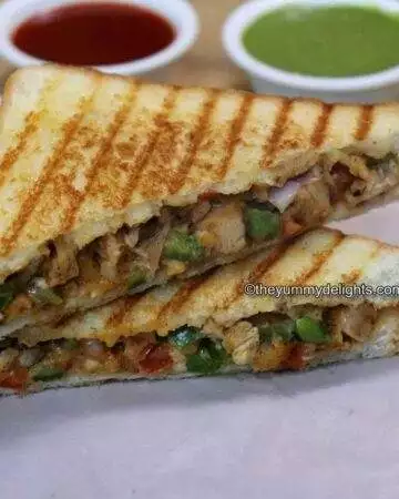 grilled chicken sandwich placed on a parchment paper. Serve with tomato sauce and green chutney on the side.