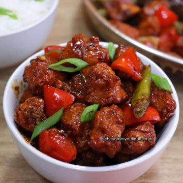 close-up of chinese chilli chicken dry served in a white bowl. It is placed on a table.