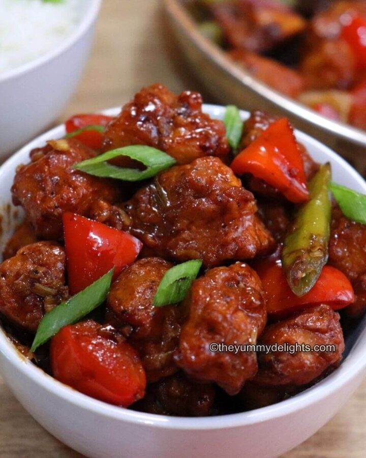 chilli chicken served in a white bowl. It is served with steamed rice.