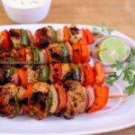 mediterranean chicken kabobs served on a white plate with lemon slice and onion rings.