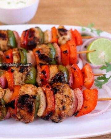 mediterranean chicken kebabs served on a white plate with lemon slice and onion rings.