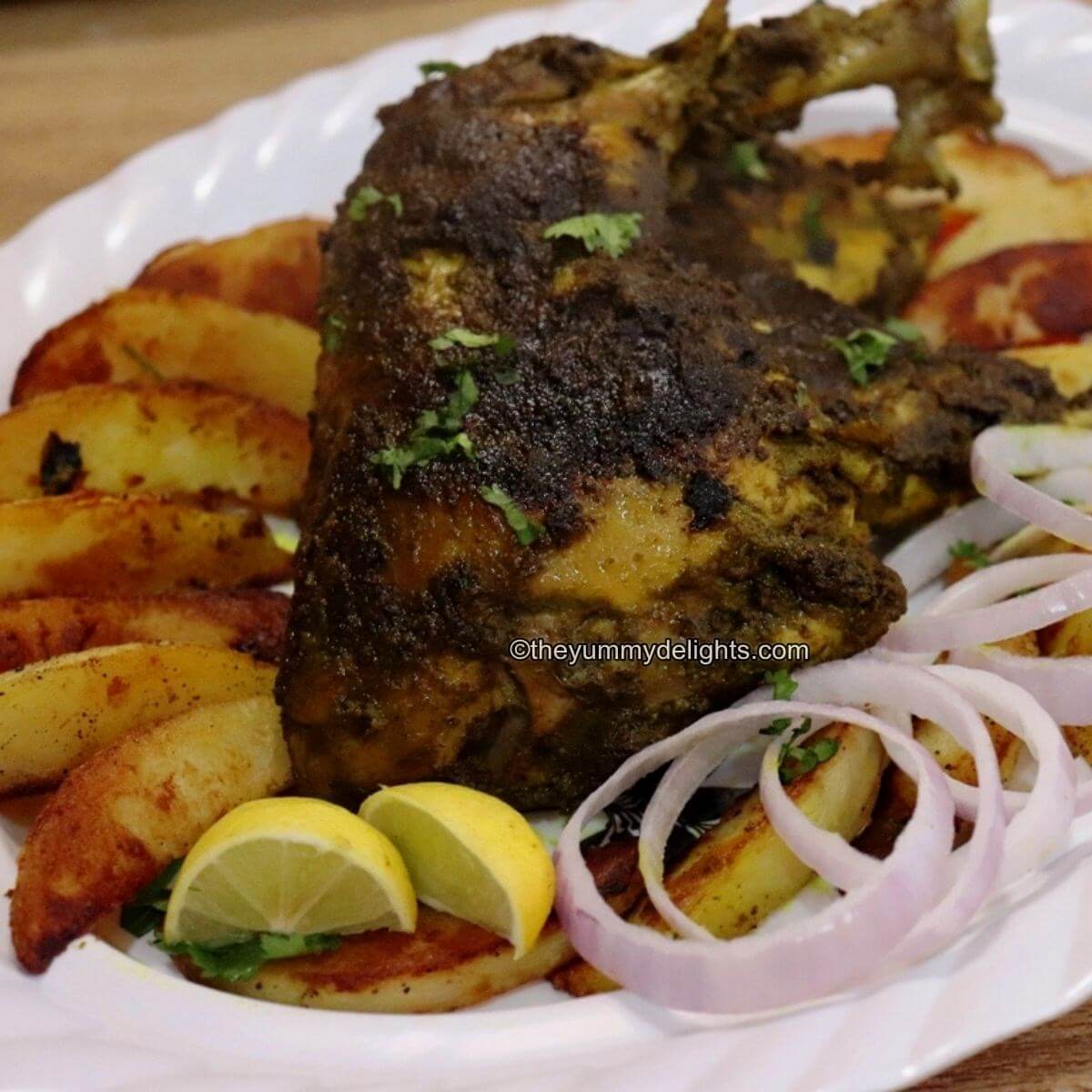 close-up of chicken cafreal served with potato wedges, onion rings, and lemon wedges on a white plate.