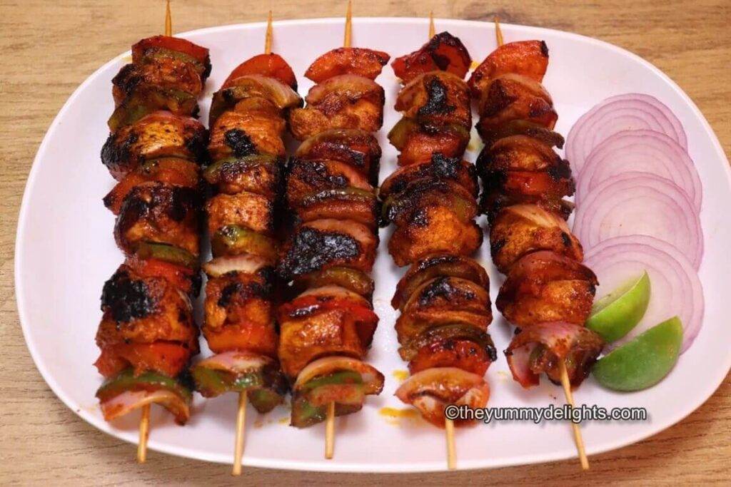 Close-up image of 5 shashlik kebabs served on a white plate with onion slices and lemon wedges.