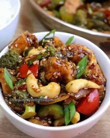 close-up of chicken and vegetable stir fry served in a white bowl.