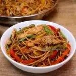 close-up of chicken stir fry with noodles in a white bowl.